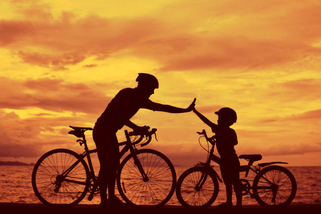 silhoutte of a man and a kid with their bikes